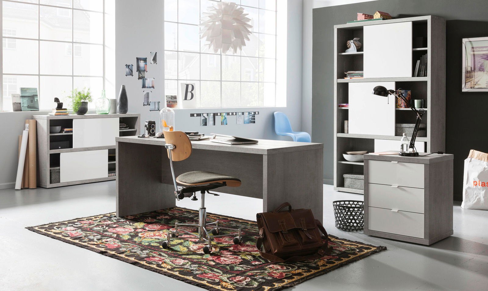 XORA Rollcontainer PUNTO Modernes Büro mit grauem Schreibtisch, Rollcontainer und Hochschrank in einem hellen Raum mit großen Fenstern, seitliche Perspektive.