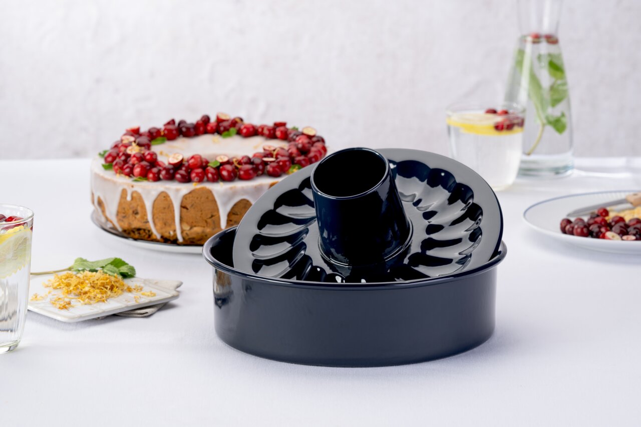 Dr. Oetker Garantieform mit flach und Rohrboden BACKLIEBE Schwarze Gugelhupfform aus Metall, seitliche Perspektive, auf einem Tisch mit einem dekorierten Kuchen im Hintergrund.