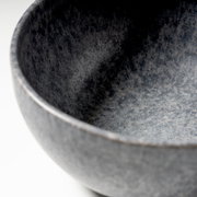 Detailaufnahme einer graublauen, gesprenkelten Keramikschale mit sichtbarer Innenfläche und Rand, fotografiert aus schräger Draufsicht