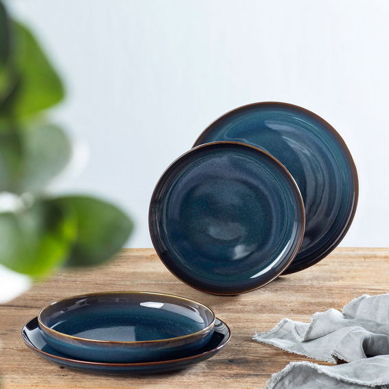 Vierteiliges Tafelset in Denim-Blau, bestehend aus zwei großen und zwei kleinen Tellern, auf einem Holztisch arrangiert. Perspektive von vorne.