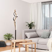 Moderne LED-Stehleuchte mit geschwungenem Design in einem gemütlichen Wohnzimmer, seitliche Perspektive.