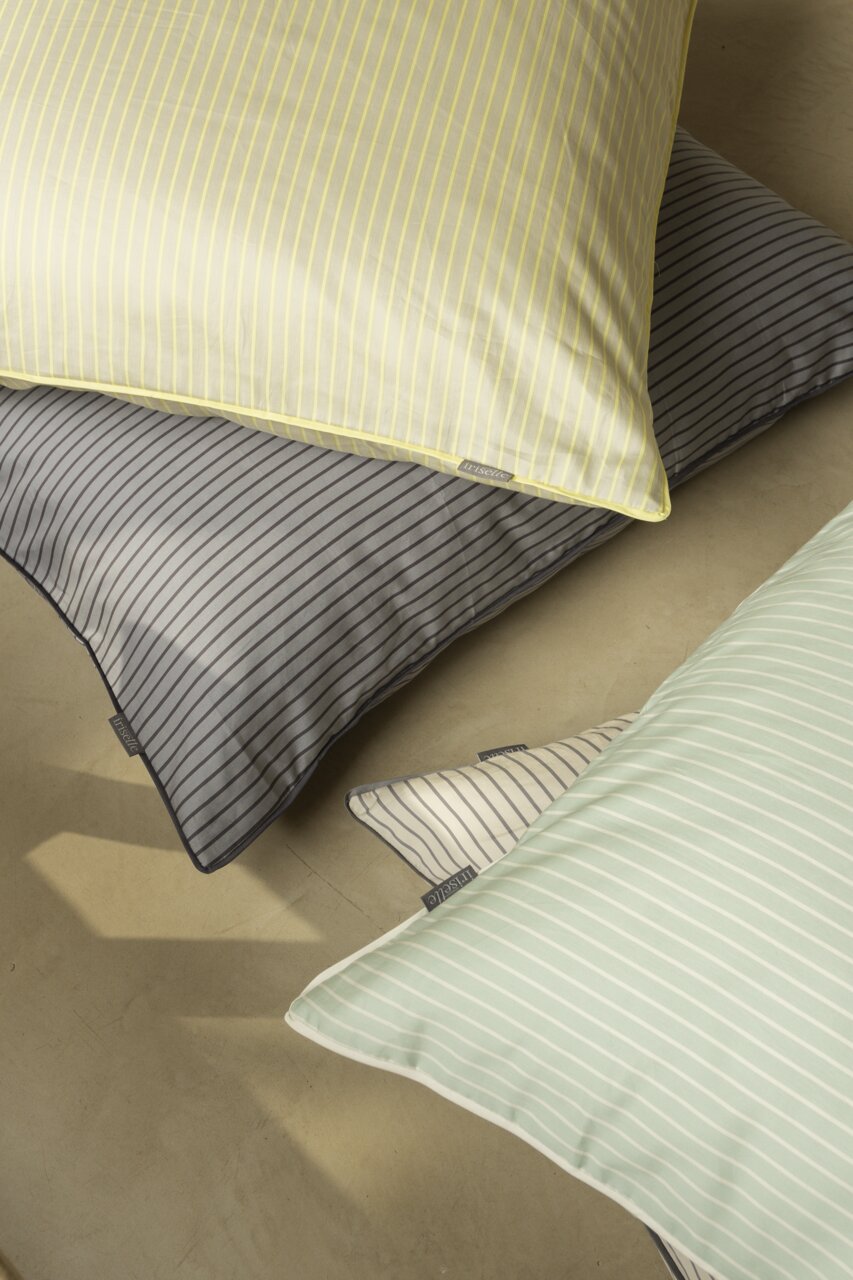 Blick von oben auf gestreifte Bettwäsche in verschiedenen Farben: Gelb, Grau, Grün und Weiß.