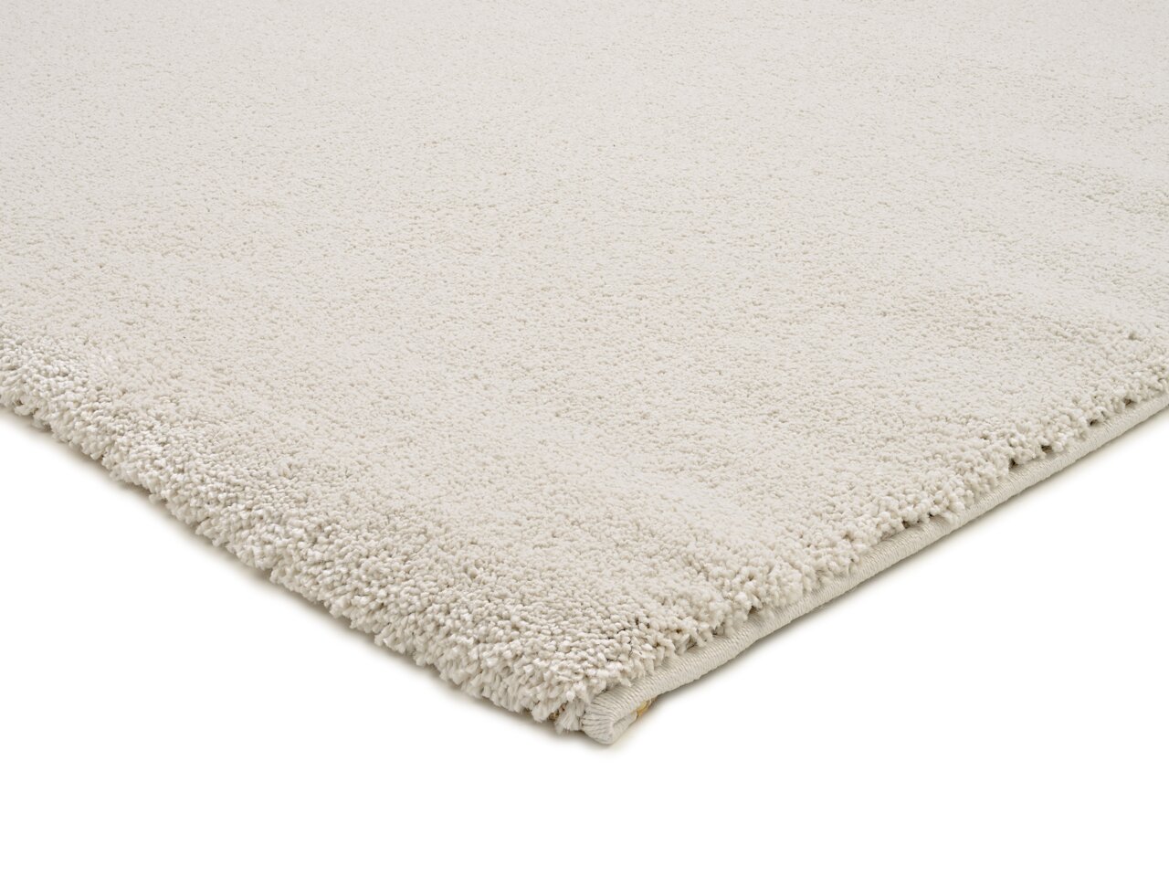 Nahaufnahme eines cremefarbenen Uni-Teppichs mit weicher, flauschiger Textur, von der Seite fotografiert.