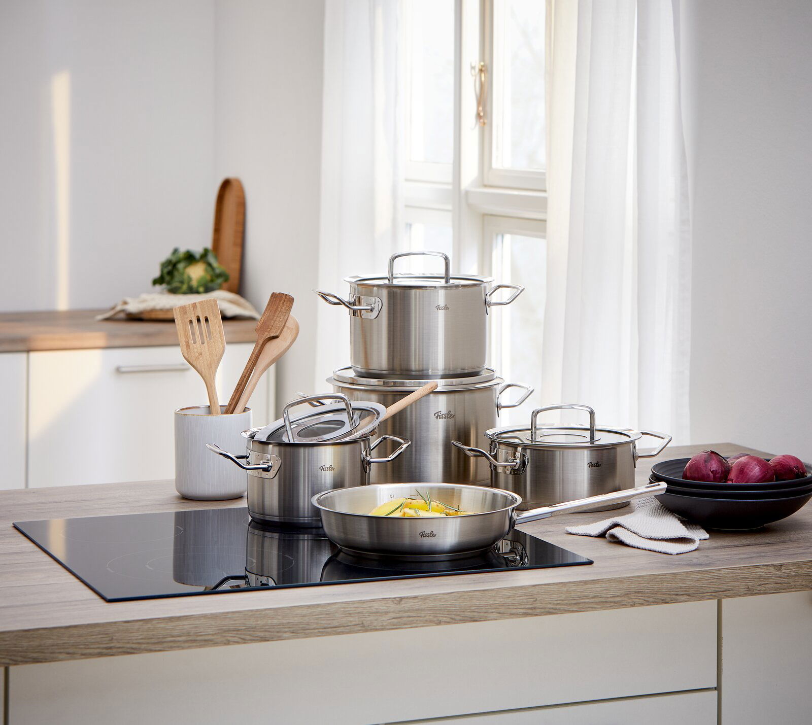 Fissler Topfset 5-tlg. ORIGINAL PROFI COLLECTION Küchenansicht mit einem 5-teiligen Topfset aus Edelstahl, bestehend aus Töpfen und Pfannen mit Glasdeckeln, auf einem modernen Herd in einer hellen Küche.