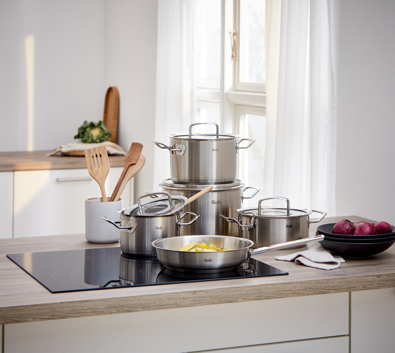 Fissler Topfset 5-tlg. ORIGINAL PROFI COLLECTION Küchenansicht mit einem 5-teiligen Topfset aus Edelstahl, bestehend aus Töpfen und Pfannen mit Glasdeckeln, auf einem modernen Herd in einer hellen Küche.