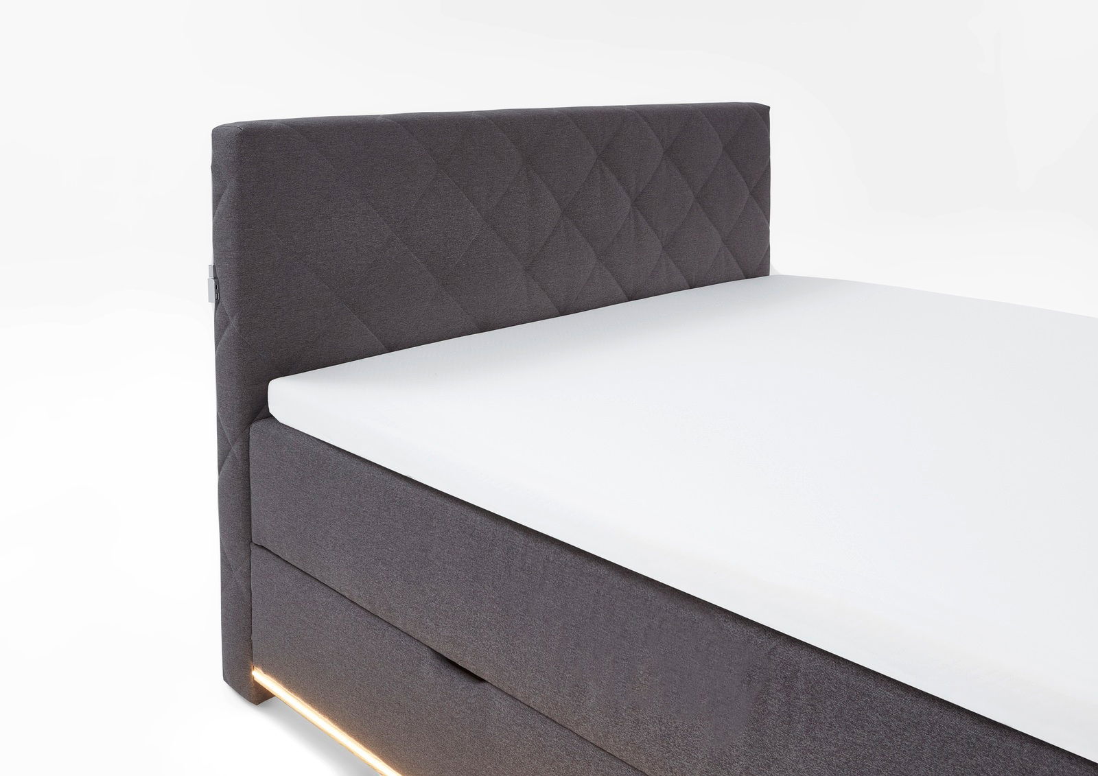 Seitliche Ansicht eines modernen Boxspringbetts mit grauem, gestepptem Kopfteil und integrierter Beleuchtung.