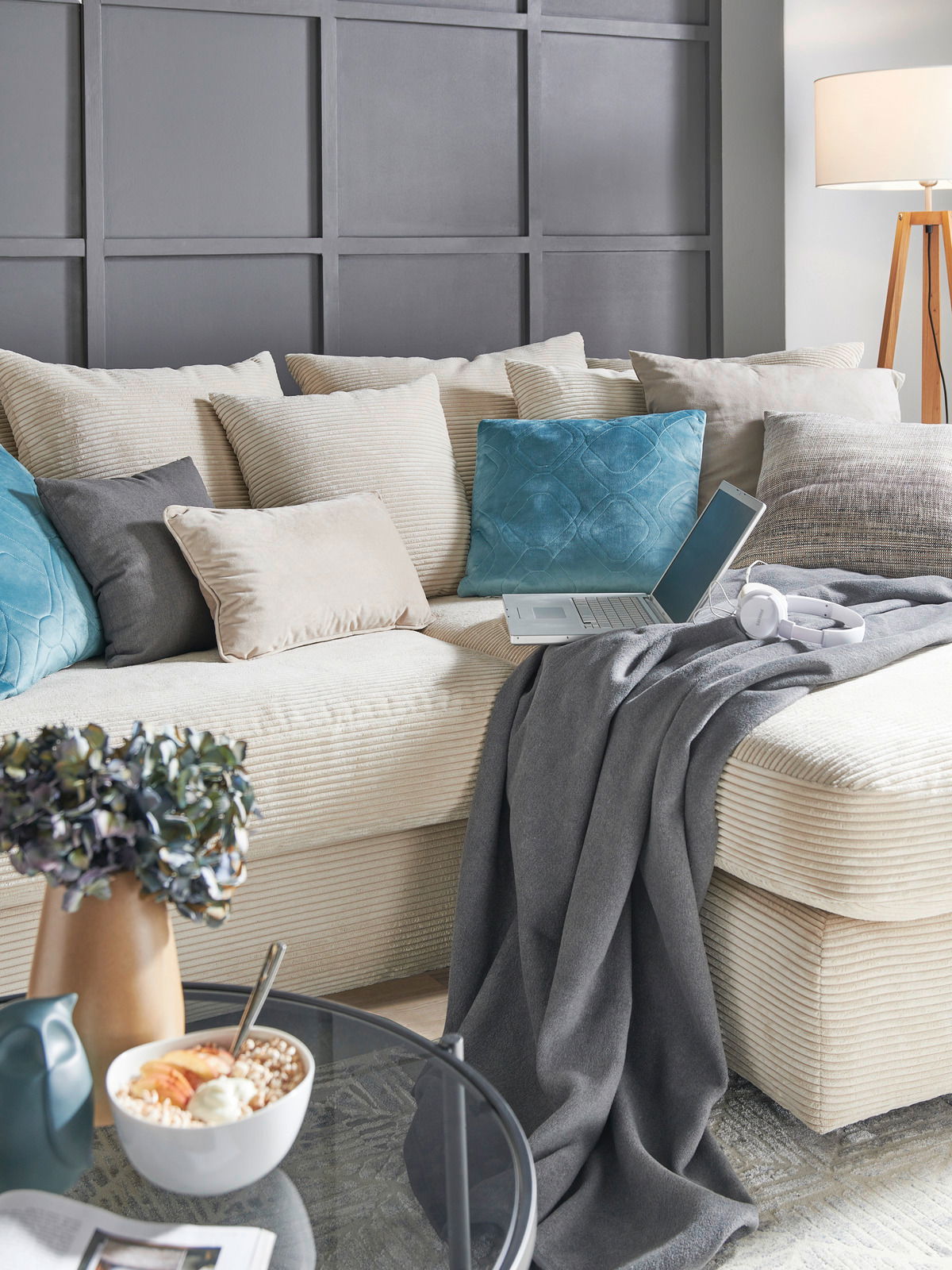 Gemütliche Rundecke mit beigen und blauen Kissen, grauer Decke und Laptop, seitliche Perspektive