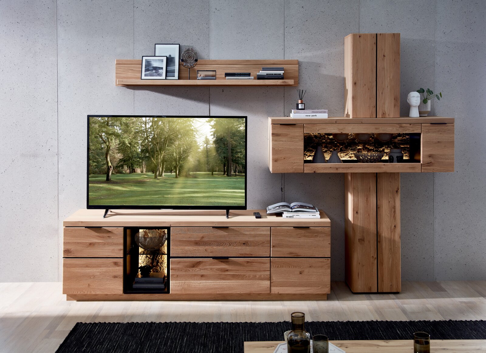 Moderne Wohnwand aus massivem Holz mit TV-Lowboard, Wandregal und Vitrine mit Glasfach und Beleuchtung, frontale Ansicht