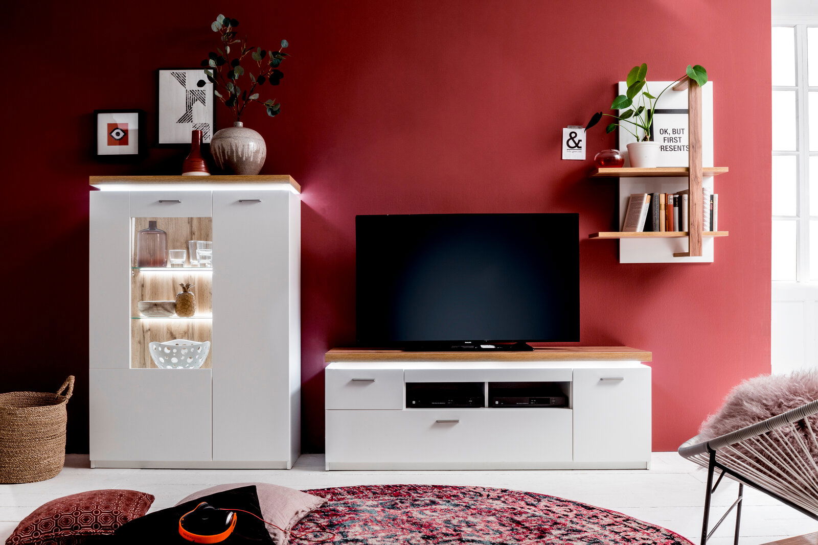 XORA Funkfernbedienungs-Set CALI Moderne Wohnzimmermöbel mit weißem Highboard, TV-Element und Wandregal vor einer roten Wand, frontal betrachtet.