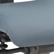 Nahaufnahme der Sitzfläche eines Drehstuhls mit grauem Stoffbezug, seitliche Perspektive.