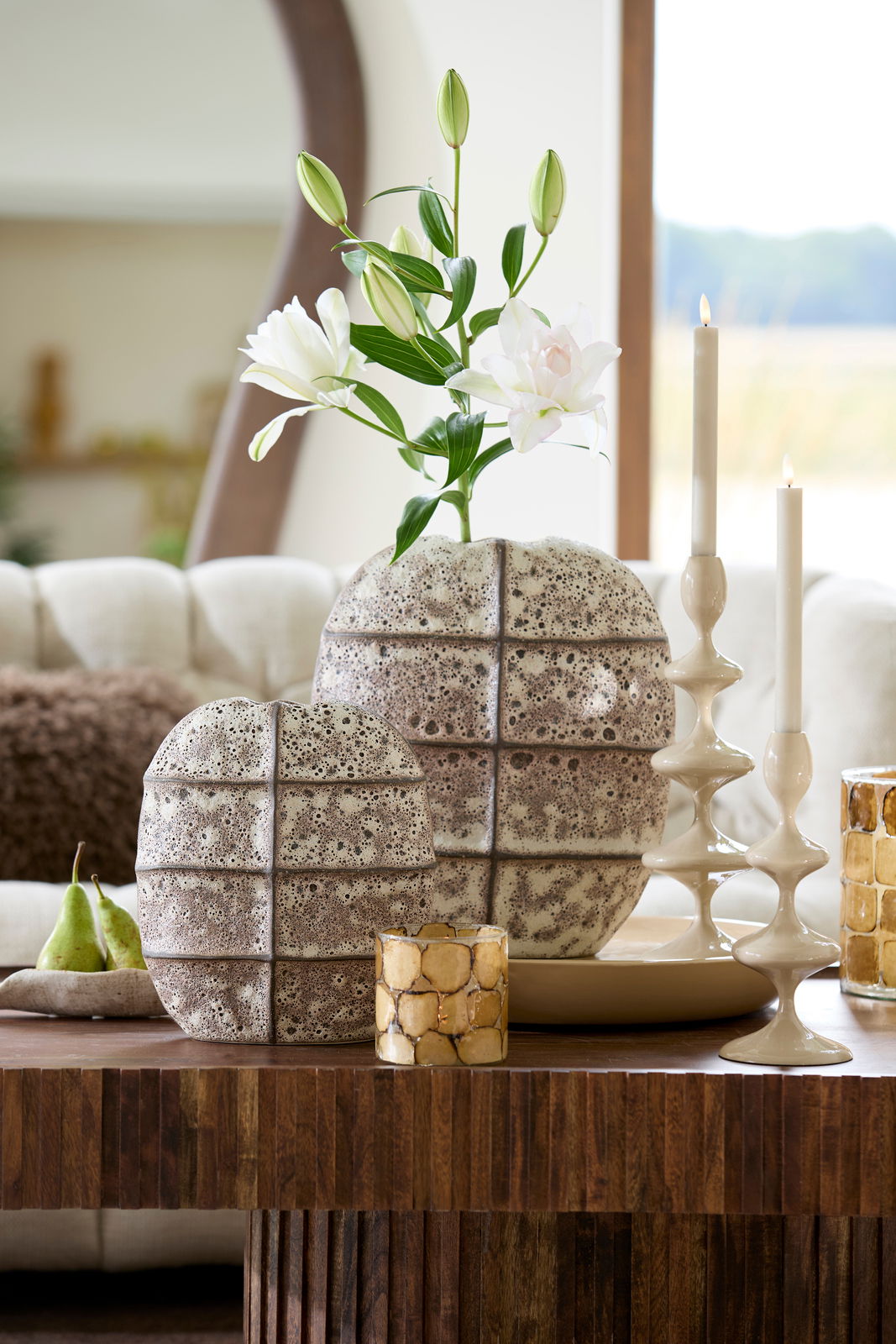 Kerzenständer in modernem Design mit zwei brennenden Kerzen, auf einem Holztisch in einem stilvoll eingerichteten Wohnzimmer, seitliche Perspektive.