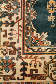 Nahaufnahme eines traditionellen Teppichs mit komplexen Mustern in Rot-, Beige- und Grüntönen. Die Perspektive zeigt eine detaillierte Ansicht der Ecke des Teppichs.