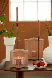 Dekorative Schale mit Früchten auf einem Tisch, umgeben von Kerzen und Vasen, aus seitlicher Perspektive fotografiert.