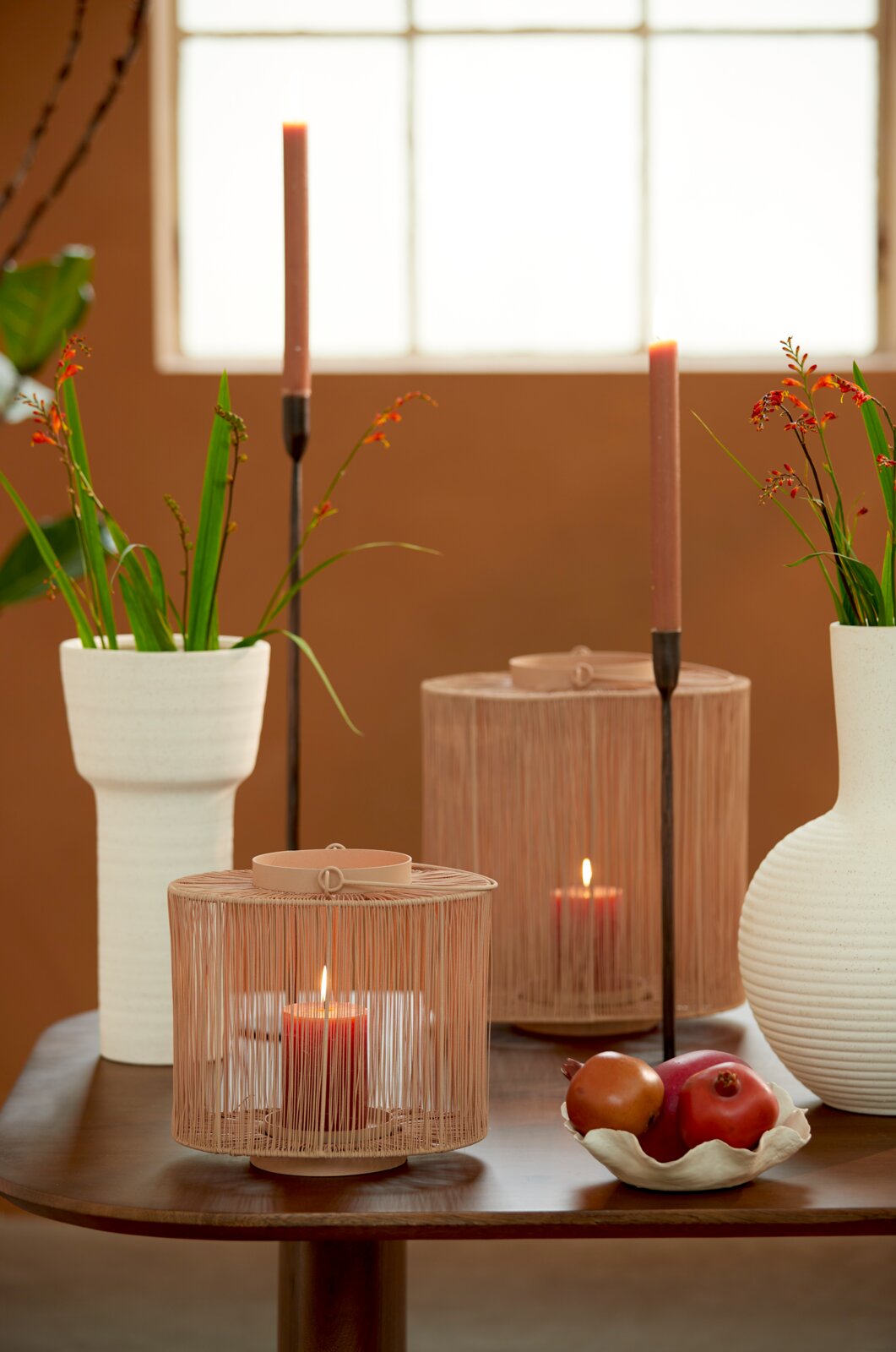 Dekorative Schale mit Früchten auf einem Tisch, umgeben von Kerzen und Vasen, aus seitlicher Perspektive fotografiert.