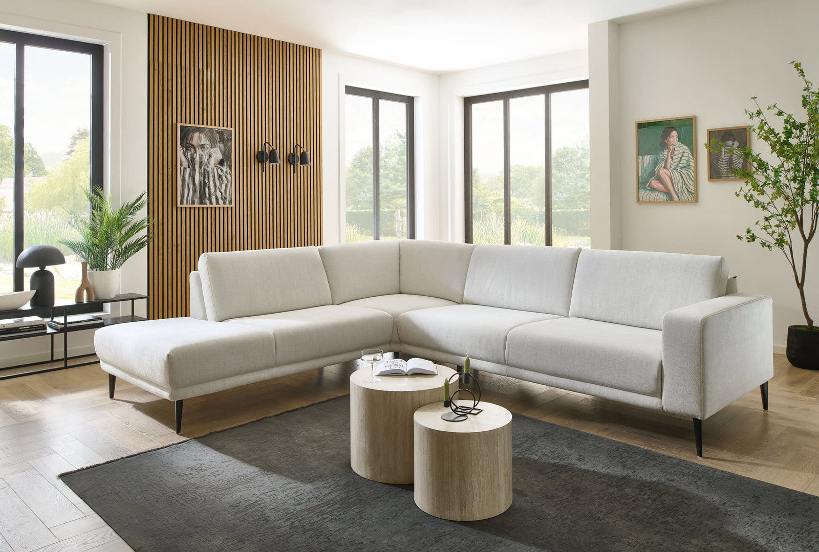 Moderne Eckgarnitur in hellem Beige, in einem stilvoll eingerichteten Wohnzimmer mit Holzboden und großen Fenstern, aus einer leicht seitlichen Perspektive fotografiert.
