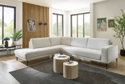 Moderne Eckgarnitur in hellem Beige, in einem stilvoll eingerichteten Wohnzimmer mit Holzboden und großen Fenstern, aus einer leicht seitlichen Perspektive fotografiert.