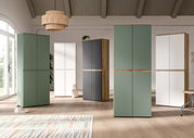 Moderne, hohe Schränke mit glatten Fronten in Grün, Weiß und Anthrazit mit Holzdetails in einem hellen Wohnraum, frontale Perspektive auf die Möbelgruppe.