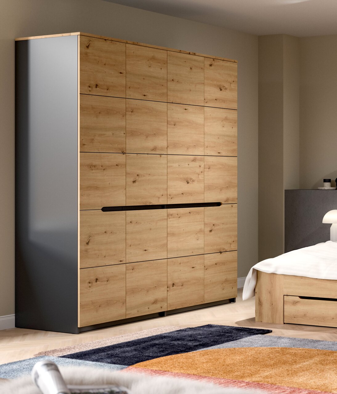 Moderner Kleiderschrank in Eiche-Optik mit dunklen Seiten und langem schwarzen Griff, im Schlafzimmer neben einem Bett, aus leicht schräger Frontansicht.