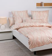 Bettwäsche-Set in Beige und Rosa mit geometrischem Muster auf einem weißen Bett, seitliche Perspektive.