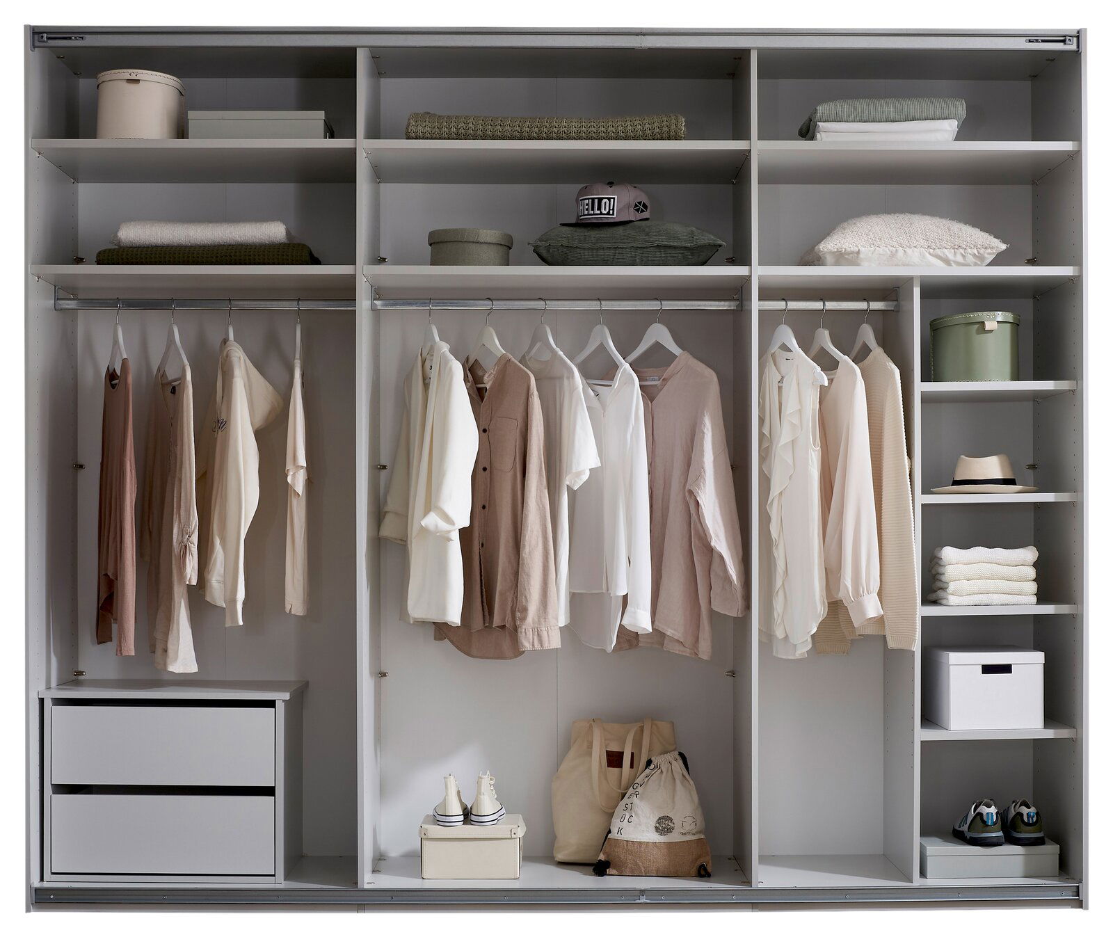 Offener weißer Kleiderschrank mit mehreren Fächern, Kleiderstangen und Schubladen, bestückt mit aufgehängter Kleidung, gefalteten Textilien, Boxen, Hüten und Schuhen; Frontansicht.