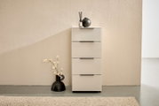 Schmaler, moderner Schubladenschrank in Creme/Beige mit vier Schubladen und schwarzen Griffleisten, frontal aus Augenhöhe vor einer strukturierten Wand fotografiert; oben Deko mit Duftdiffusor und schwarzer Vase, daneben schwarze Bodenvase mit Blüten.