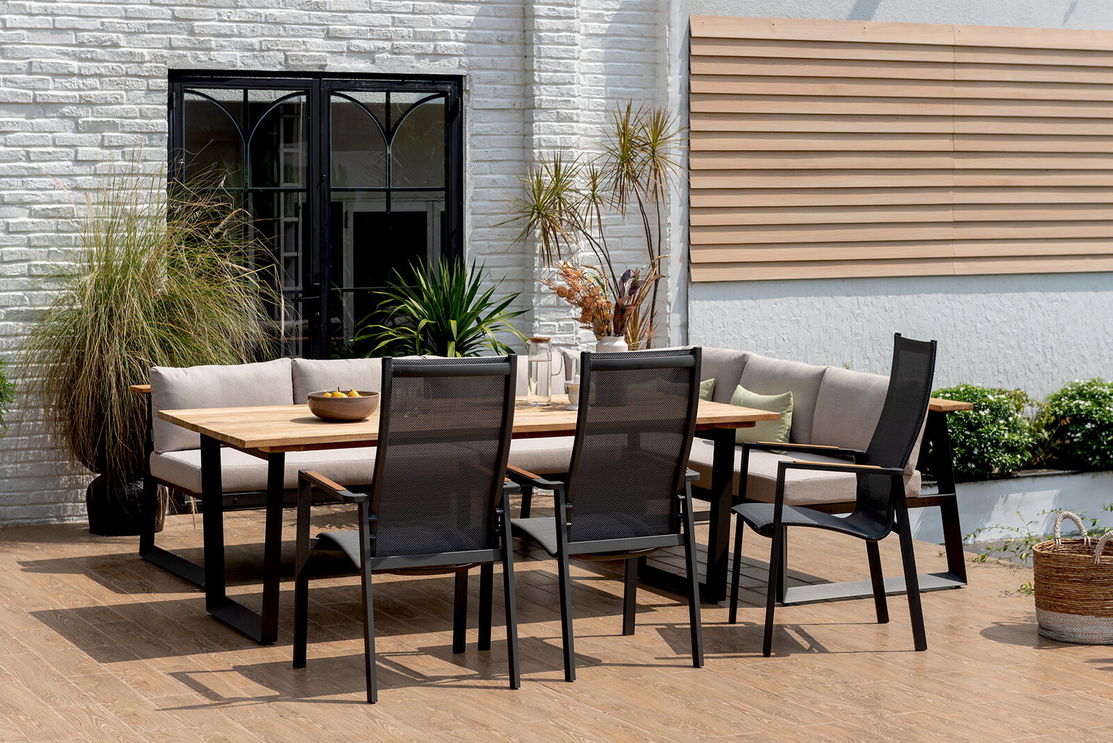 Gartenmöbel-Set mit Holztisch und schwarzen Stühlen, umgeben von Pflanzen, aus der Perspektive von vorne.