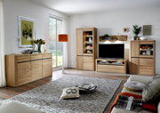 Modernes Wohnzimmer mit einem Sideboard aus Holz, das links im Raum steht. Die Perspektive zeigt das Sideboard von vorne, umgeben von stilvoller Dekoration und einem großen Fenster im Hintergrund.
