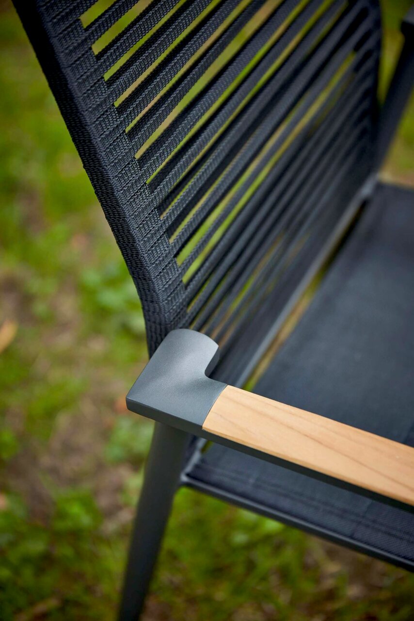 Nahaufnahme eines Sessels mit schwarzer, geflochtener Rückenlehne und Armlehne aus Holz und Metall, von schräg oben fotografiert.