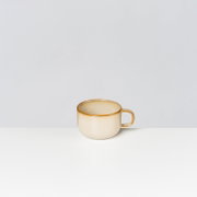 Beige Keramik-Tasse mit goldenem Rand und Henkel, freigestellt vor hellem Hintergrund, seitliche Frontansicht leicht von oben