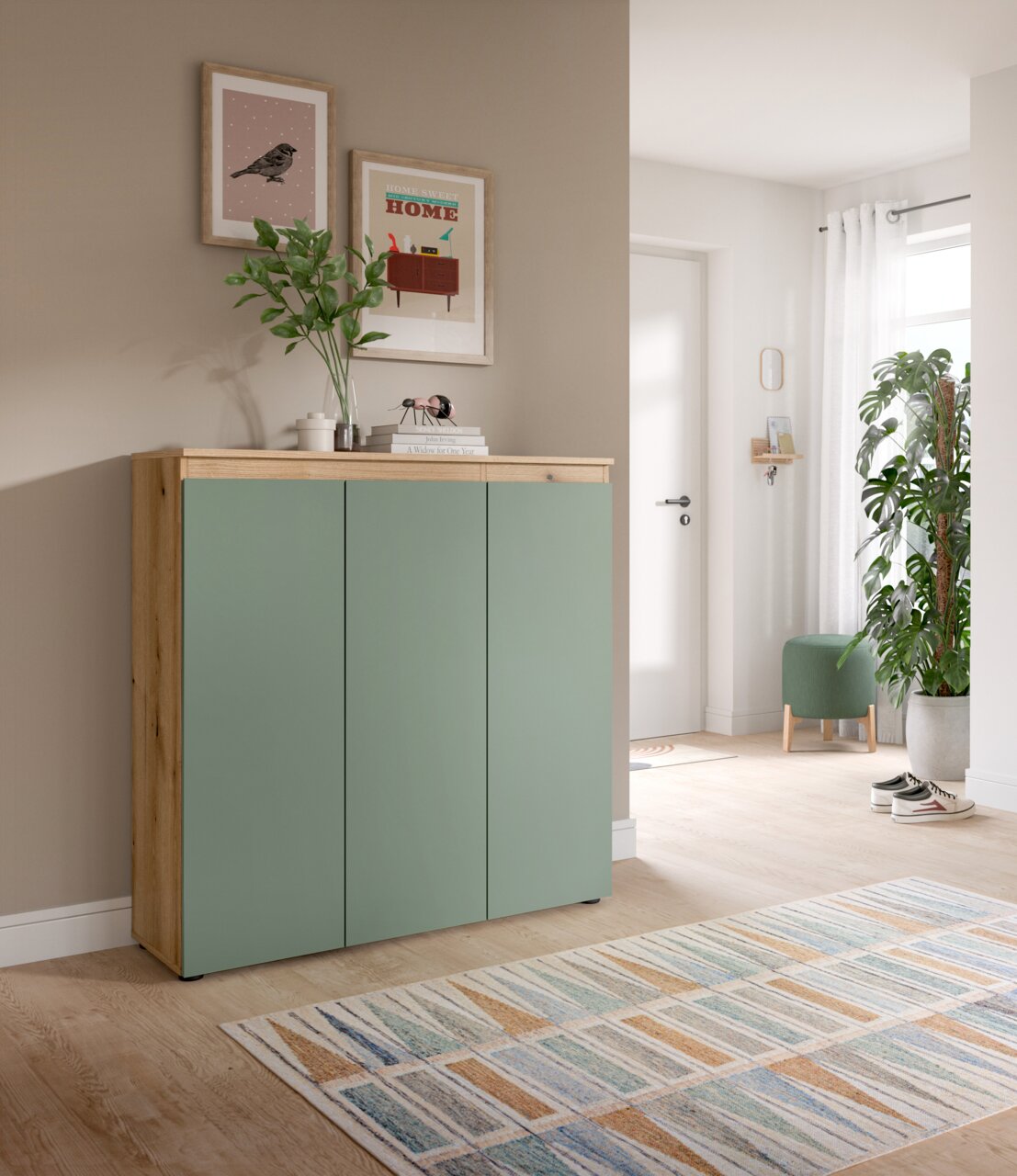 Modernes Sideboard/Schuhschrank mit drei grün-matten Fronten und Korpus in Holzoptik, im Flur vor beiger Wand, perspektivisch schräg von vorn links fotografiert.