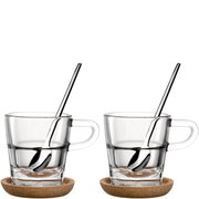 Zwei Espressotassen aus Glas mit Griff, jeweils auf einem Untersetzer aus Kork, mit einem Löffel im Inneren, seitliche Perspektive.