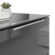 Nahaufnahme einer modernen Nachtkommode mit glänzender Oberfläche, silbernem Griff und Dekorationen wie Bücher und einer kleinen Pflanze auf der Oberseite.