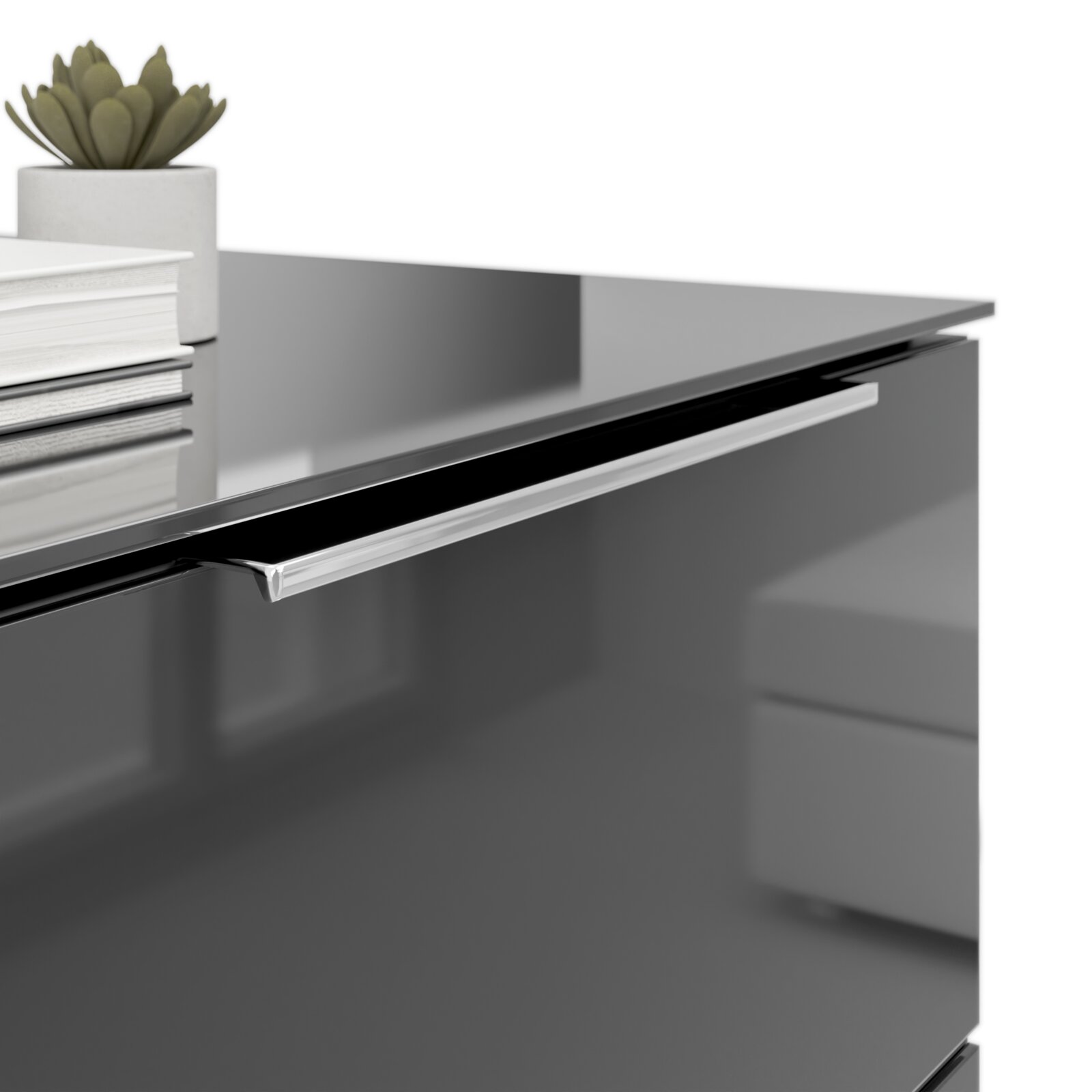 Nahaufnahme einer modernen Nachtkommode mit glänzender Oberfläche, silbernem Griff und Dekorationen wie Bücher und einer kleinen Pflanze auf der Oberseite.