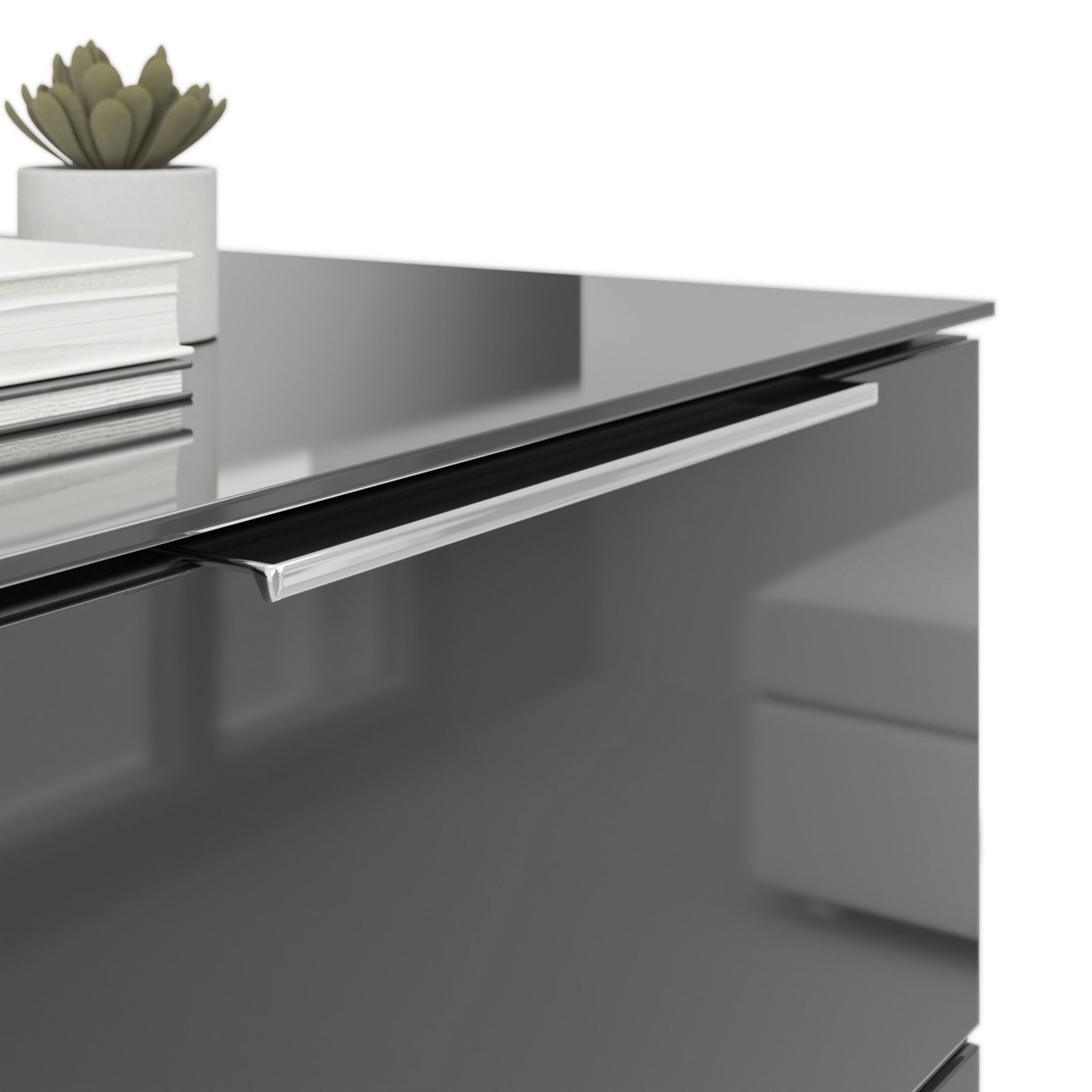 Nahaufnahme einer modernen Nachtkommode mit glänzender Oberfläche, silbernem Griff und Dekorationen wie Bücher und einer kleinen Pflanze auf der Oberseite.