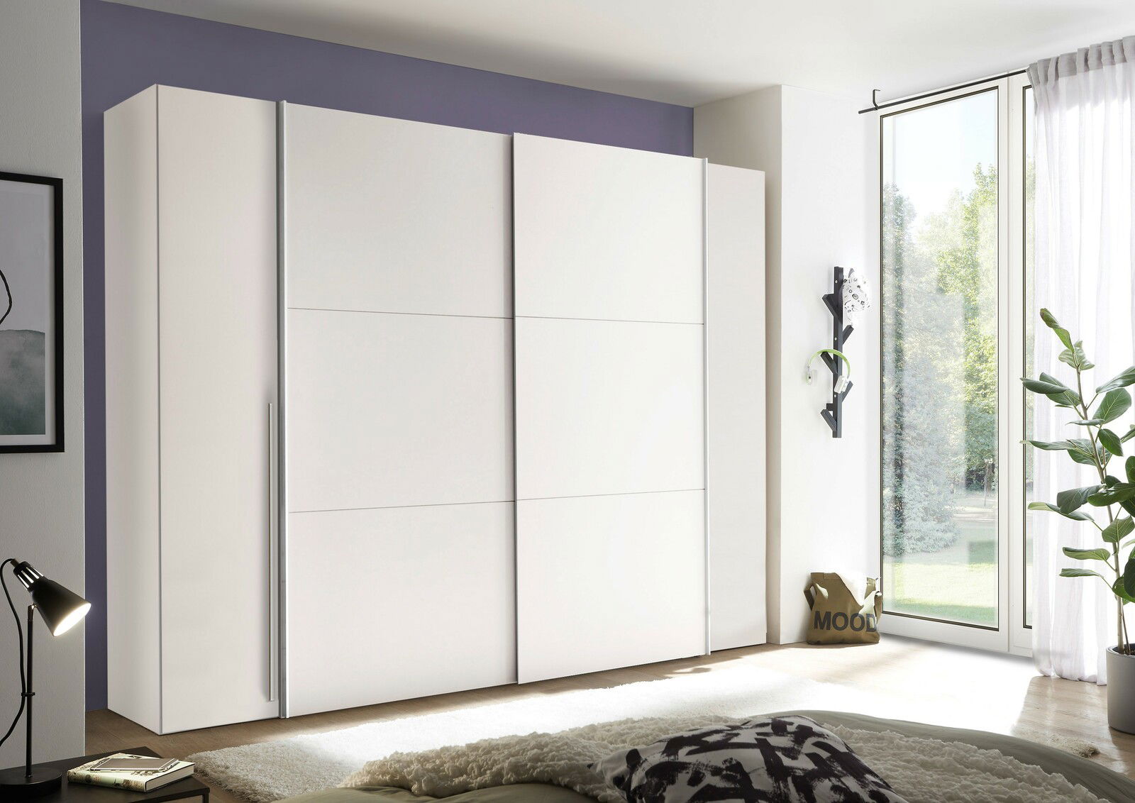 Moderner weißer Dreh- und Schwebetürenschrank mit vier Türen, seitliche Perspektive, in einem hellen Raum mit großen Fenstern.