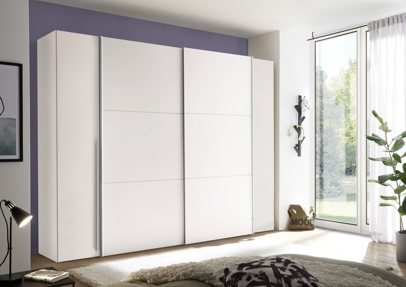 Moderner weißer Dreh- und Schwebetürenschrank mit vier Türen, seitliche Perspektive, in einem hellen Raum mit großen Fenstern.