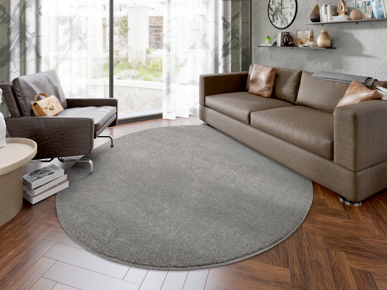 Runder grauer Uni-Teppich in einem modernen Wohnzimmer mit braunem Sofa und Sessel, Blick aus der Vogelperspektive.