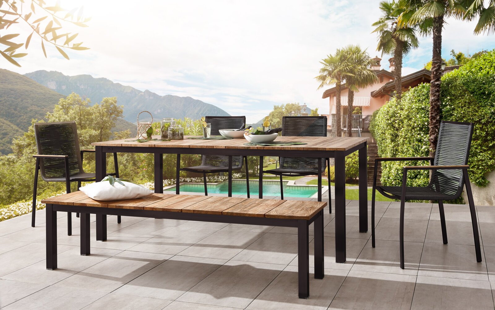 Moderner Gartensessel aus Metall und Holz, Teil einer stilvollen Terrassenmöbelgruppe mit Blick auf einen Pool und eine malerische Berglandschaft.