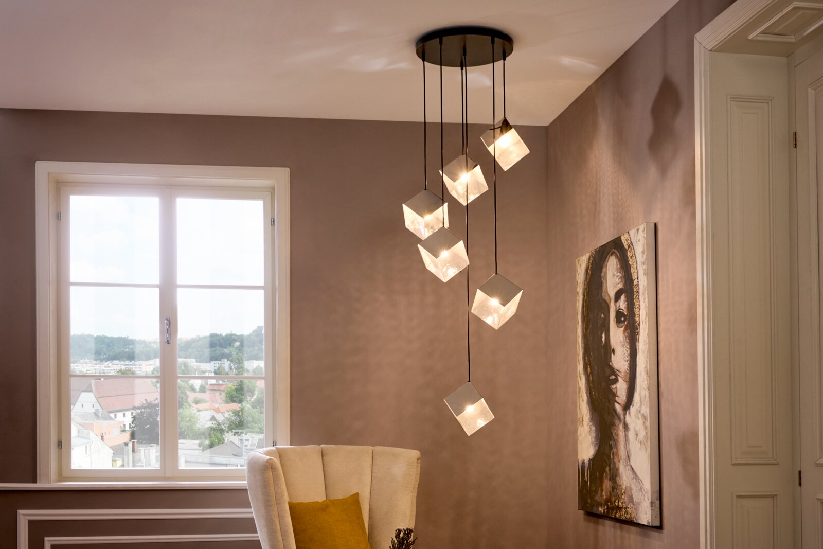 Moderne hanglamp met zes kubusvormige glazen kappen aan zwarte kabels en een ronde plafondplaat, die een warme gloed verspreidt in een woonkamer; schuin van onderaf gezien (onderzicht)
