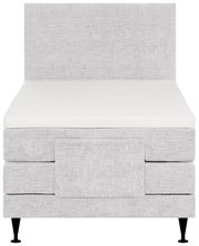 Vooraanzicht van een luxe lichtgrijze gestoffeerde boxspring met hoog hoofdbord, witte matras en zwarte poten.
