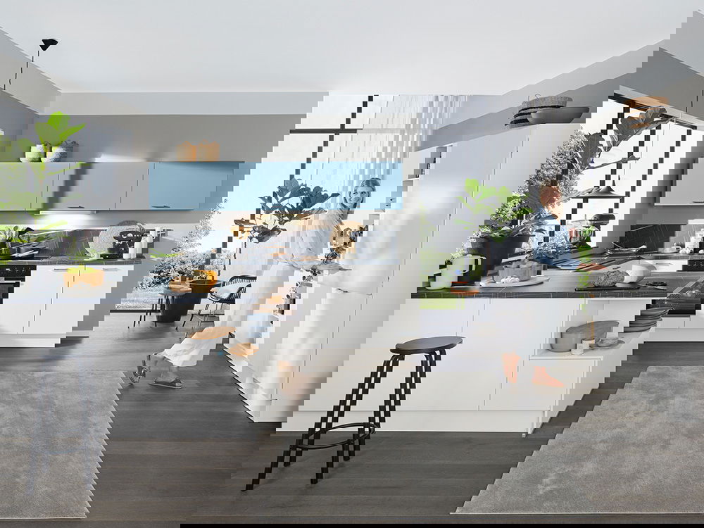 Helle, moderne Küche mit weißen Unterschränken, himmelblauen Oberschränken, dunkler Arbeitsplatte und großen Fensterfronten.