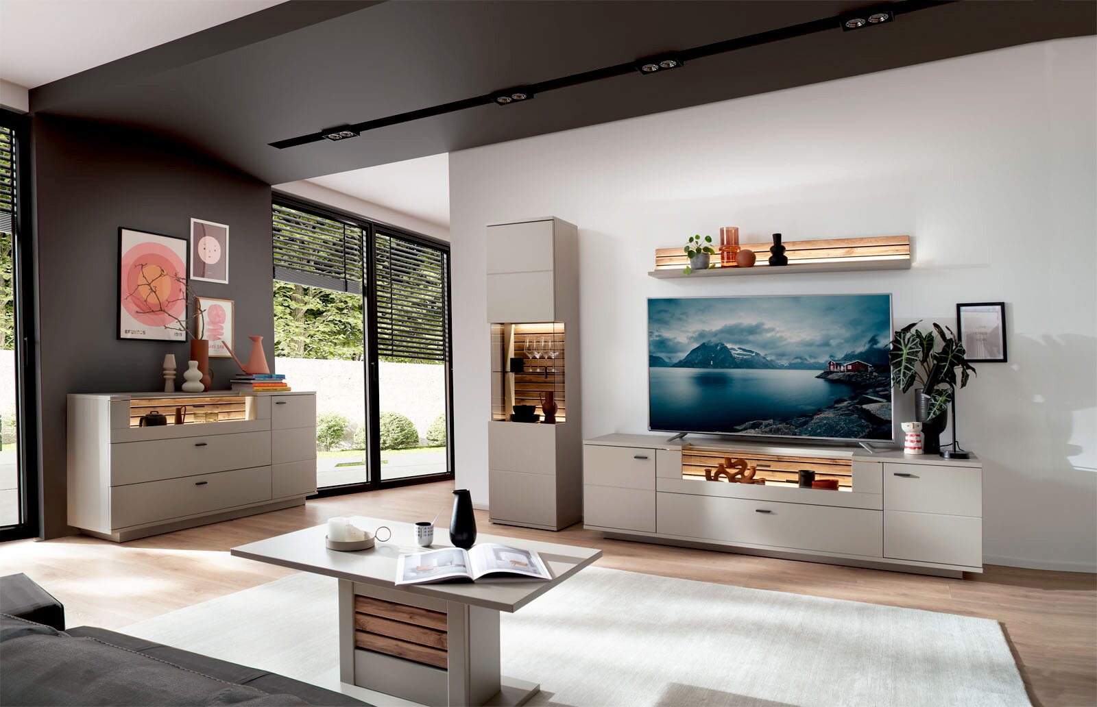 Modernes Wohnzimmer mit heller Wohnwand und TV-Board in Beige mit Holz-Akzenten und LED-Beleuchtung, Vitrine und Sideboard, aufgenommen aus leicht schräger Frontperspektive im Weitwinkel.