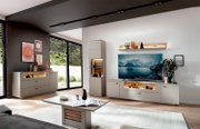 Modernes Wohnzimmer mit heller Wohnwand und TV-Board in Beige mit Holz-Akzenten und LED-Beleuchtung, Vitrine und Sideboard, aufgenommen aus leicht schräger Frontperspektive im Weitwinkel.