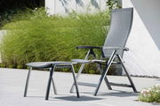 Moderner Klappsessel mit Fußhocker in einem Garten, seitliche Perspektive.
