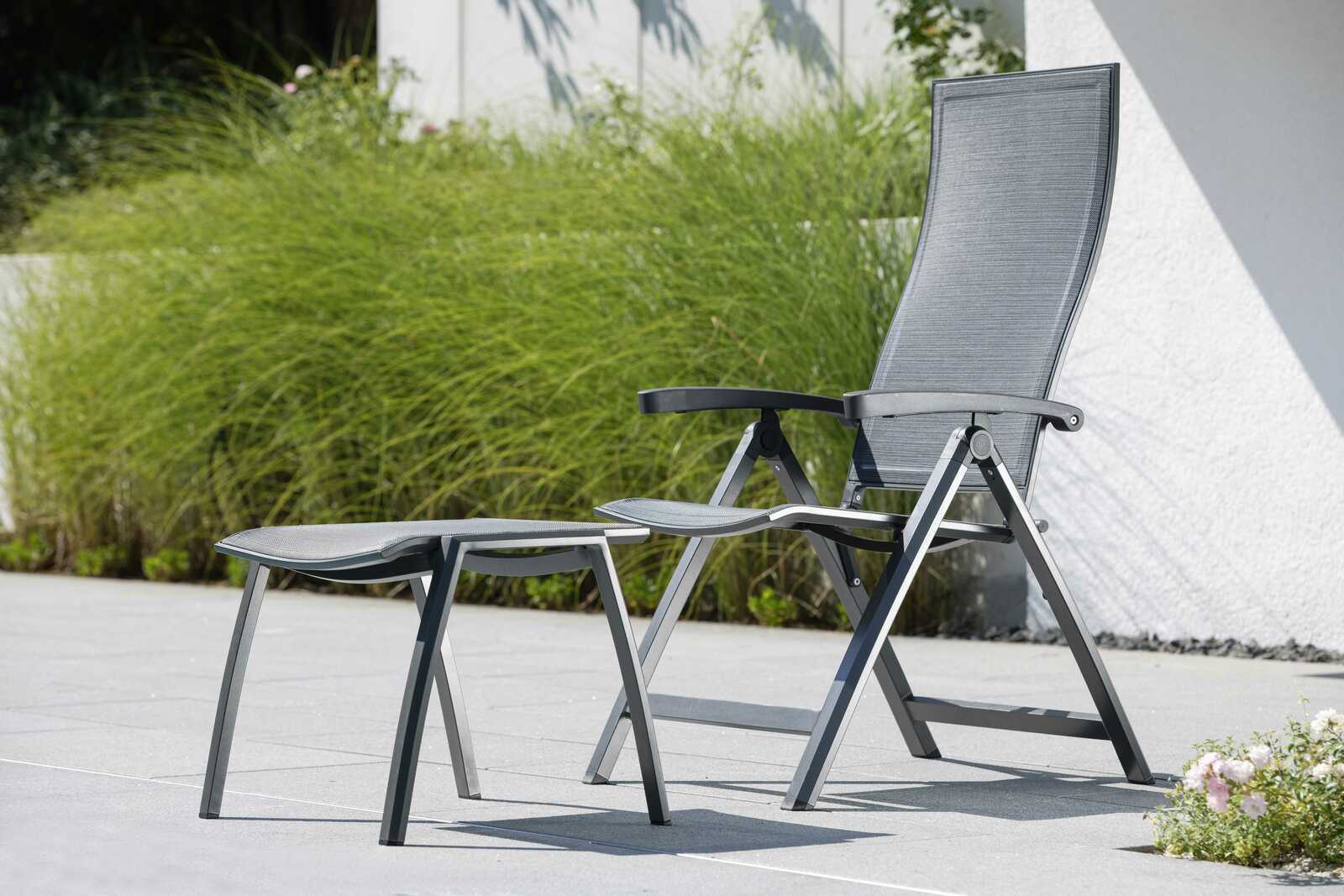 Moderner Klappsessel mit Fußhocker in einem Garten, seitliche Perspektive.