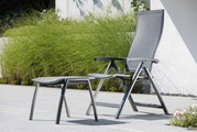 Moderner Klappsessel mit Fußhocker in einem Garten, seitliche Perspektive.