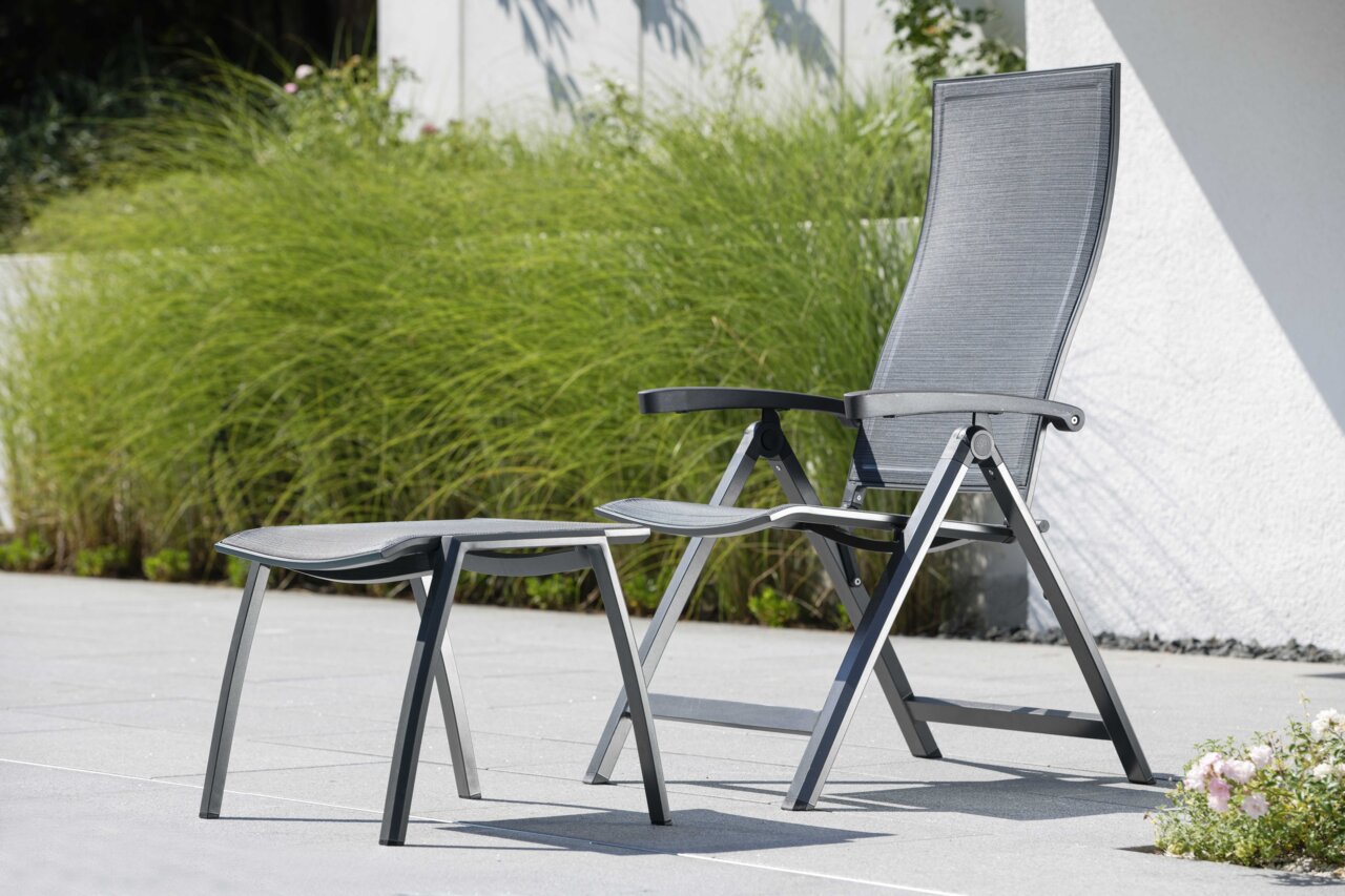 Moderner Klappsessel mit Fußhocker in einem Garten, seitliche Perspektive.