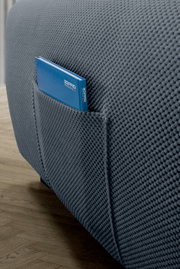 Nahaufnahme einer grauen, strukturierten Sofaecke mit einer praktischen Seitentasche, die ein blaues Buch enthält. Perspektive von der Seite.