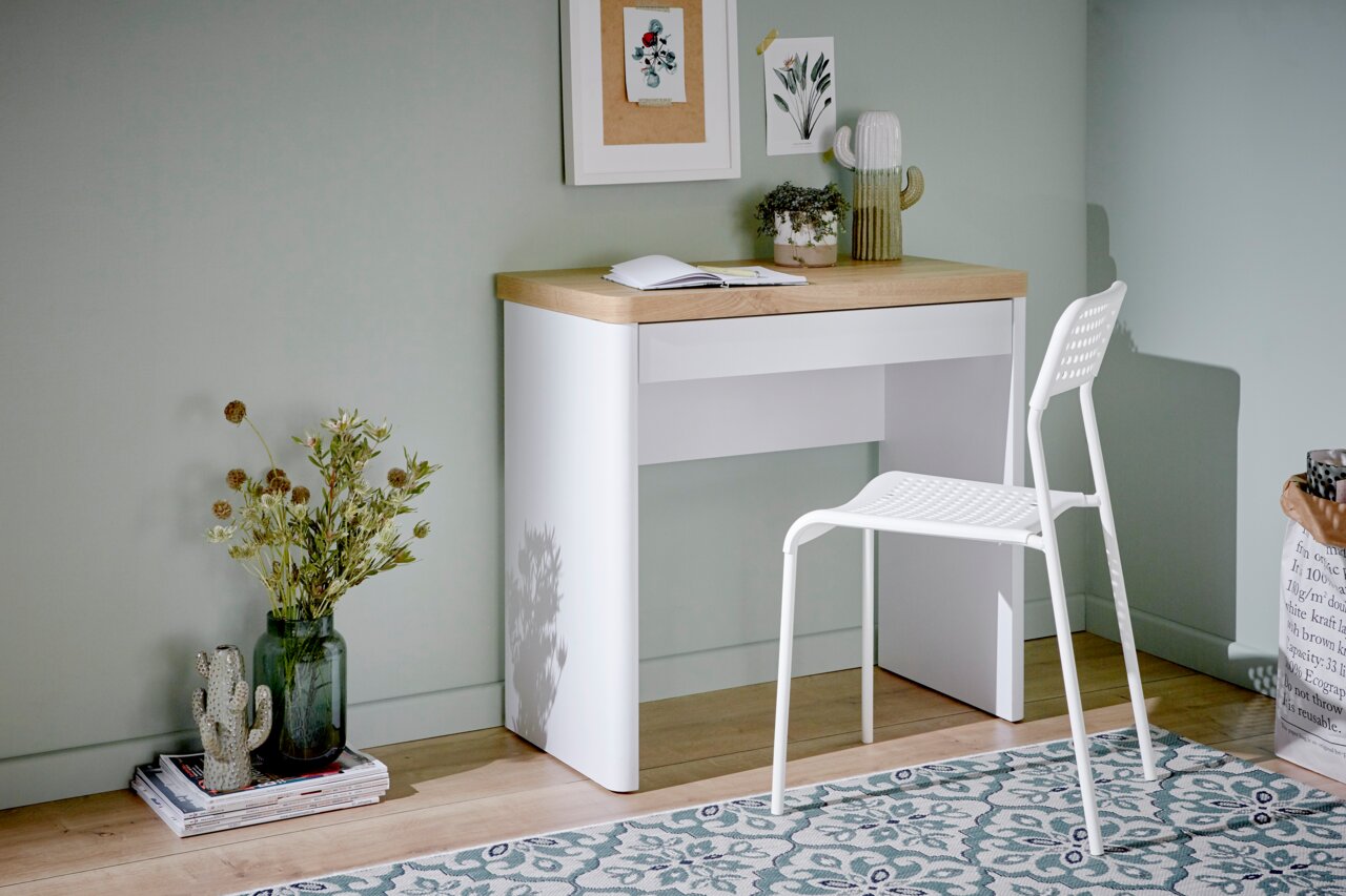 Moderner Schreibtisch mit weißem Gestell und Holzplatte, seitliche Perspektive, dekoriert mit Pflanzen und Büchern.