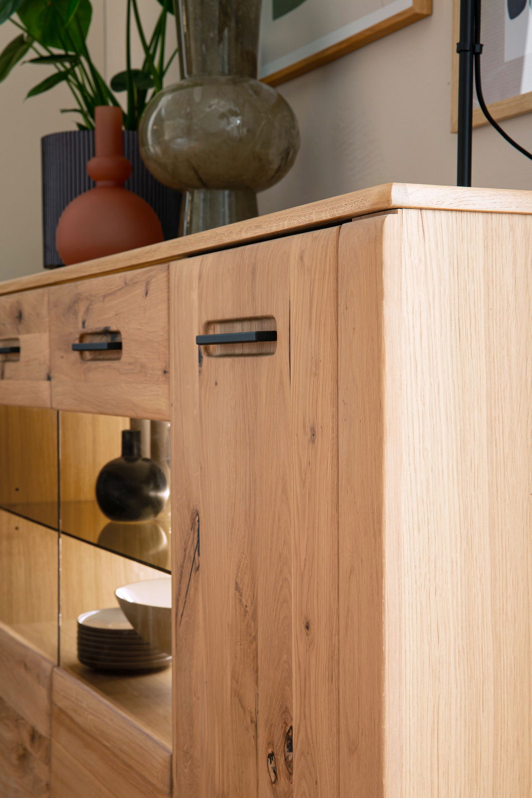 Nahaufnahme eines modernen Sideboards aus hellem Holz mit schwarzen Griffen, dekoriert mit Vasen und Pflanzen, seitliche Perspektive